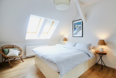 A open spacious serene bedroom with whit walls, linens and natural wood tones in room