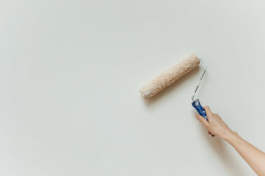 Painting a wall a neutral soft white color with a roller brush